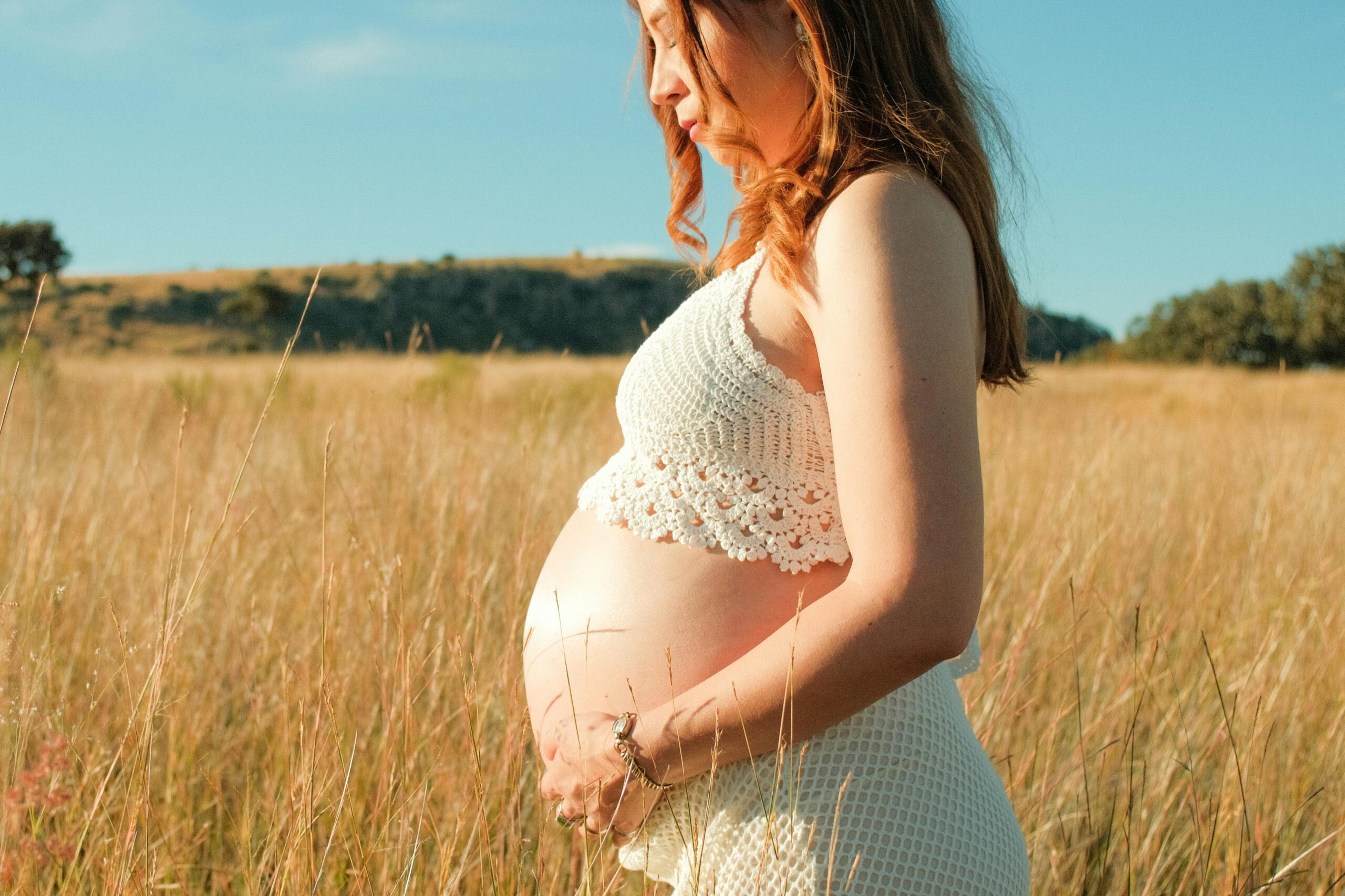 Cosa faccio A pregnant woman standing in a sunny field, embracing the beauty of motherhood.